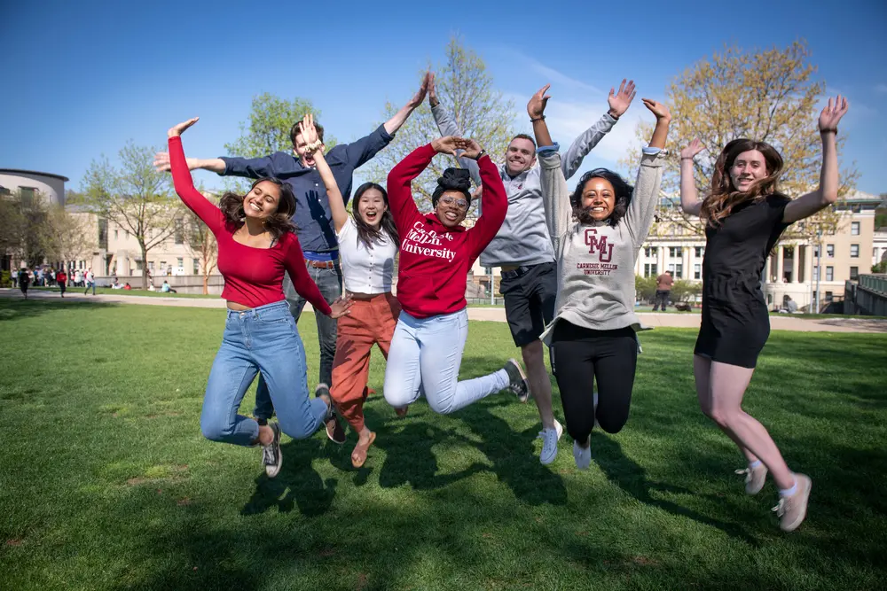 Students on the CMU lawn jumping with hands in the air