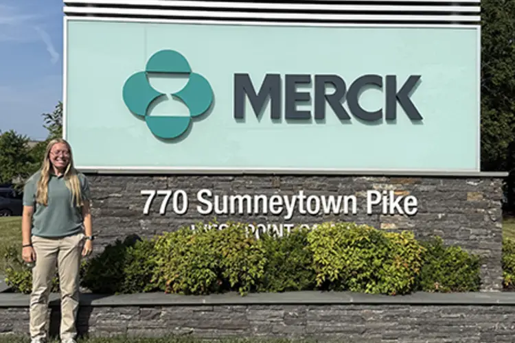 A student standing in fron of the Merck sign